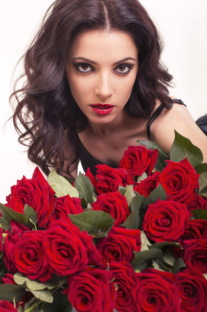 Beautiful woman with dark curly hair with bouquet of red roses - Fotoğraf, Görsel