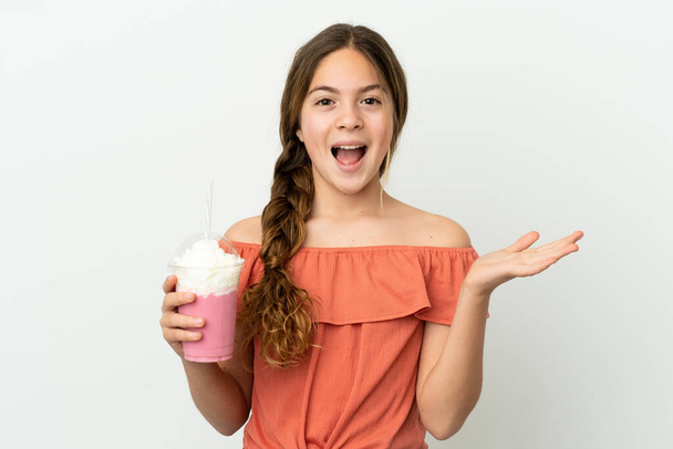 Маленька біла дівчинка з полуничним молочним коктейлем ізольована на білому тлі з шокованим виразом обличчя
 - Фото, зображення