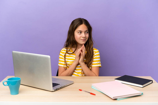 Little student girl in a workplace with a laptop isolated on purple background scheming something - Φωτογραφία, εικόνα