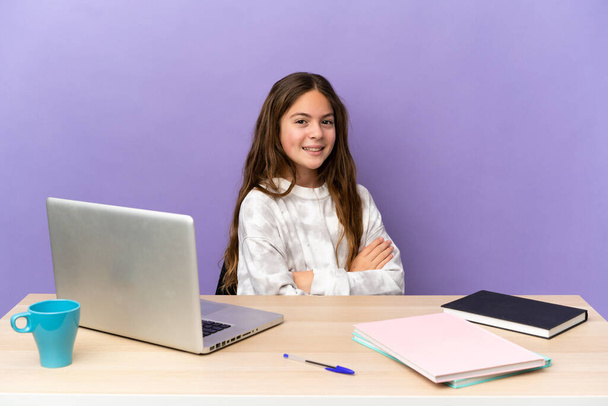 Niña estudiante en un lugar de trabajo con un ordenador portátil aislado sobre fondo púrpura con los brazos cruzados y mirando hacia adelante - Foto, Imagen