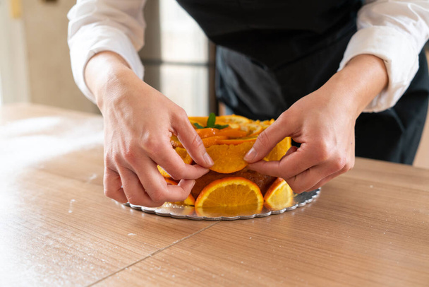 Young pastry chef cooking an orange cake with sliced oranges - Фото, зображення