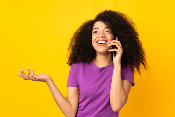 Молода афроамериканська жінка через ізольований фон, підтримуючи розмову з кимось по мобільному телефону. - Фото, зображення