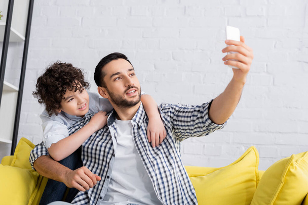 sonriente árabe hombre tomando selfie en celular con alegre hijo - Foto, imagen