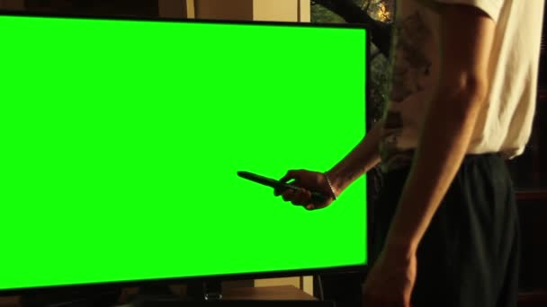 Mann mit Fernbedienung und einem Fernseher mit grünem Bildschirm. Sie können den grünen Bildschirm durch das gewünschte Filmmaterial oder Bild ersetzen. Sie können dies mit dem Keying-Effekt in After Effects oder jeder anderen Videobearbeitungssoftware tun (siehe Tutorials auf YouTube).).  - Filmmaterial, Video