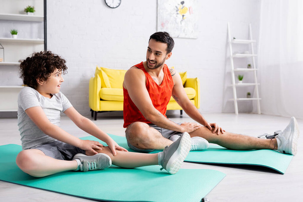 Treinamento positivo de pai e filho muçulmano em tapetes de fitness em casa  - Foto, Imagem