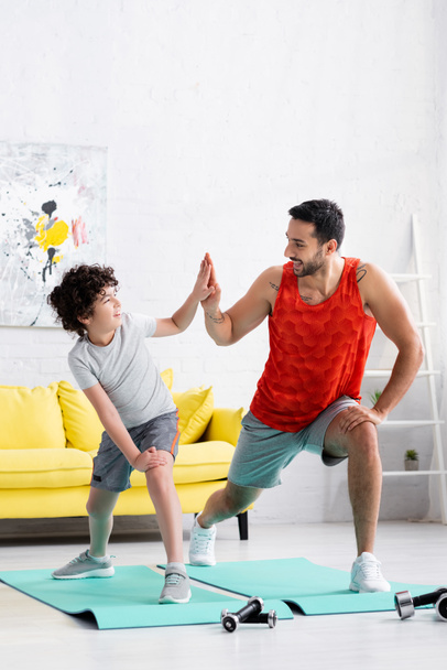 Positieve moslim vader geven high five naar zoon tijdens het trainen op fitness matten thuis  - Foto, afbeelding