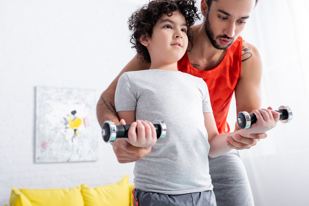 Arab férfi segít fia súlyzókkal edzés közben otthon  - Fotó, kép