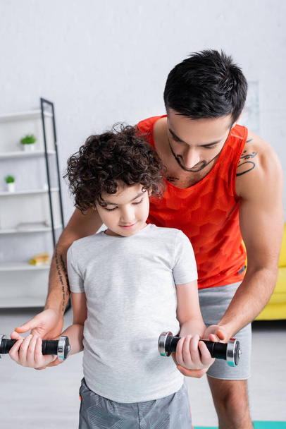 Arabian father holding dumbbell near son during home work out  - Photo, Image