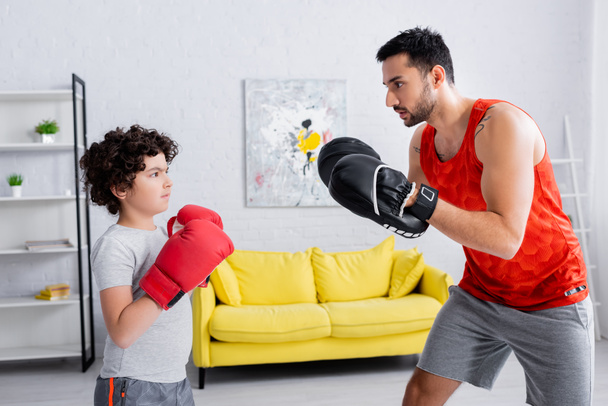 家庭で父と一緒に運動するボクシンググローブのイスラム教徒の息子  - 写真・画像