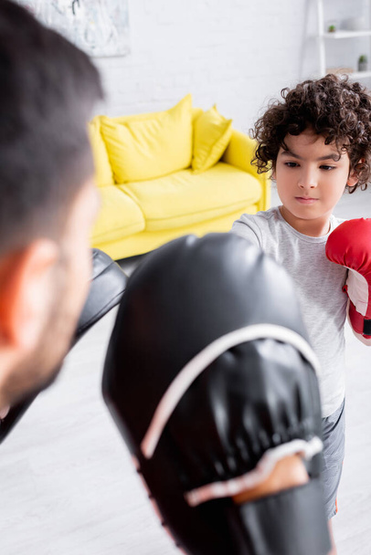 Moslim jongen boksen tijdens de training met vader in punch mitts op wazig voorgrond  - Foto, afbeelding