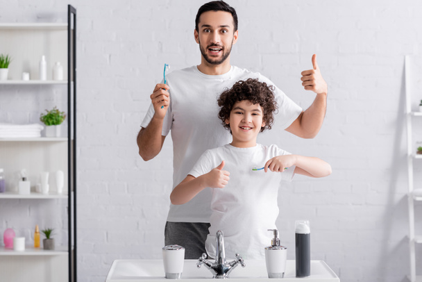 Arabe fils et père montrant comme tout en tenant des brosses à dents dans la salle de bain  - Photo, image