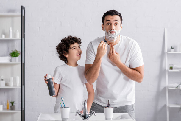 Arab férfi borotválkozás szakáll közel mosolygó fia hab a fürdőszobában  - Fotó, kép