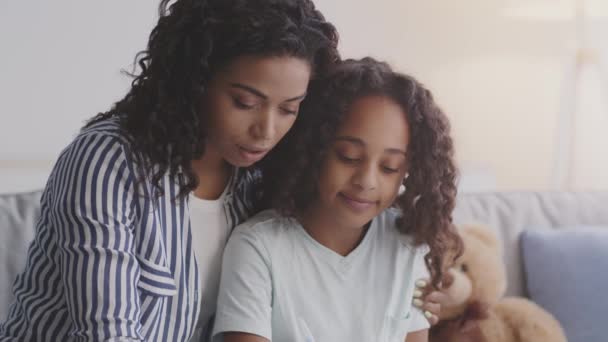 Fröhliche afrikanisch-amerikanische Mutter hilft ihrer Tochter bei den Hausaufgaben, schreibt gemeinsam in Textbüchern, Kamerafahrt - Filmmaterial, Video
