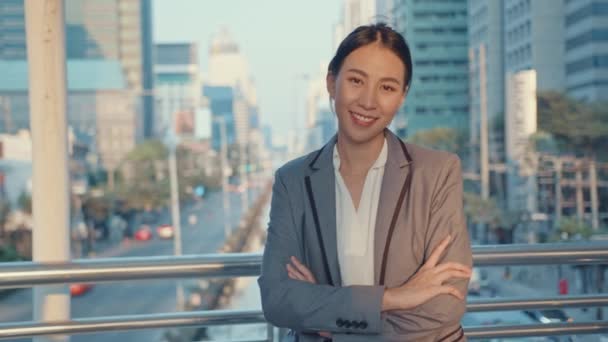 Successful young Asia businesswoman in fashion office clothes smiling and looking at camera while happy standing alone outdoors in urban modern city in the morning. Business on the go concept. - Footage, Video