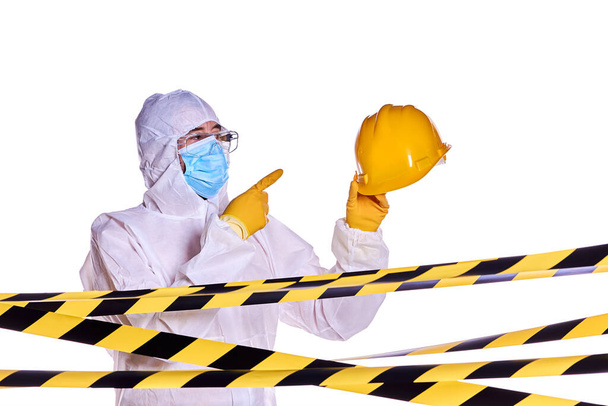 Εργάτης υγείας για πανδημία του ιού της κορώνας, φορώντας προστατευτικά ρούχα, δείχνοντας το προστατευτικό του κράνος και κρατώντας το ψηλά στον αέρα. - Φωτογραφία, εικόνα