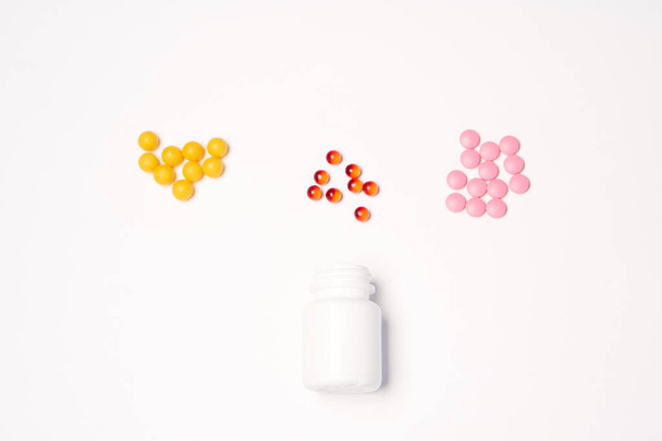 Ein Glas mit bunten Pillen, die in einer bestimmten Reihenfolge auf einem hellen Hintergrund angeordnet sind. - Foto, Bild
