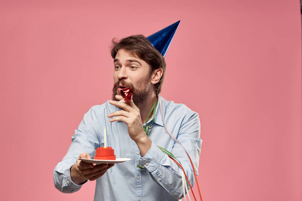 Bearded man with cake tongue on a pink background cropped view and a blue cap on his head - Photo, Image