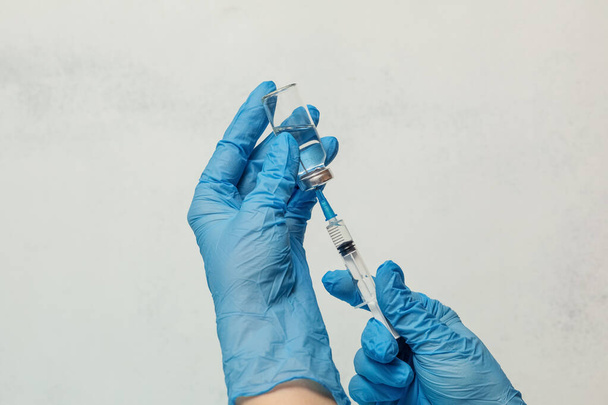 μια σύριγγα και μια φιάλη εμβολιασμού στα χέρια μιας γυναίκας με μπλε ιατρικά γάντια στο φόντο ενός ελαφρού τοιχώματος. την αρχή της συλλογικής ασυλίας από το covid19 - Φωτογραφία, εικόνα