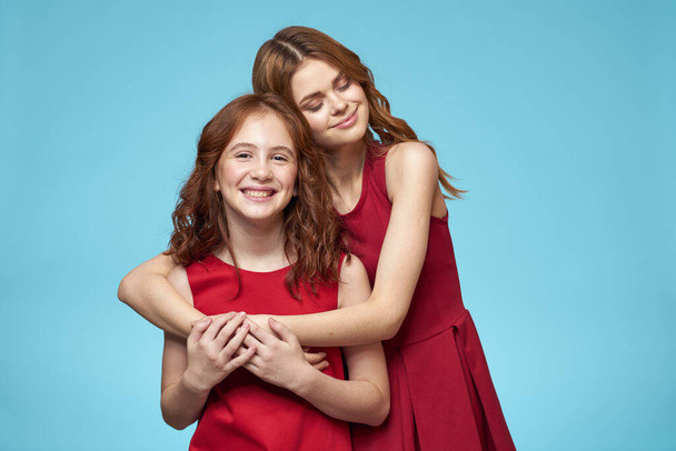 Moeder en dochter in rode jurken entertainment lifestyle leuk studio blauw achtergrond - Foto, afbeelding