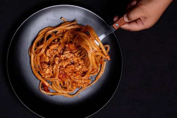 Spaghetti with tomato sauce and minced chicken. The hand is holding a fork to scoop the spaghetti. - Photo, Image