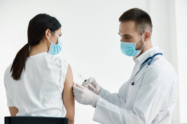 γιατρός σε λευκό παλτό ένεση μια γυναίκα ώμου εμβολιασμός προστατευτικά γάντια - Φωτογραφία, εικόνα