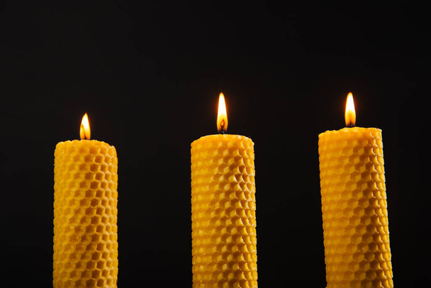 Tres velas de cera de abejas amarillas están sobre la mesa. Producto ecológico sobre un fondo oscuro - Foto, Imagen