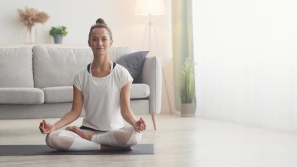 Pokój i harmonia. Wewnętrzny portret młodej spokojnej damy medytującej w domu, siedzącej w pozycji lotosu, wolnej przestrzeni - Materiał filmowy, wideo