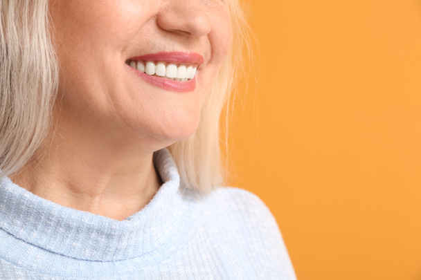 Happy mature woman with beautiful smile on color background, closeup - Photo, Image