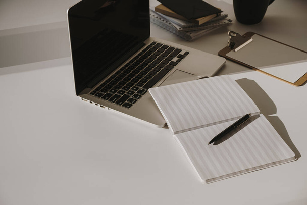 Laptop na mesa com xícara de café, folha de papel contra a parede branca. Espaço de trabalho minimalista do escritório em casa. - Foto, Imagem