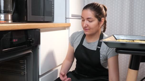 Nuori nainen laittaa leivinpaperin evästeillä uuniin - Materiaali, video