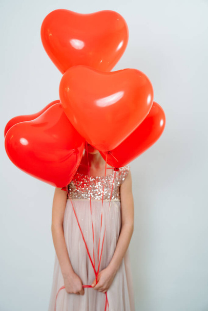 teen girl face closed red balloons of hearts near white wall - Foto, afbeelding