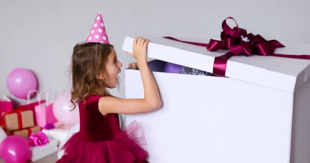 Gioiosa bambina in abito rosa e cappello aperto grande confezione regalo con palloncini a casa festeggiamenti festivi, Buon compleanno. Festeggiamenti - Filmati, video