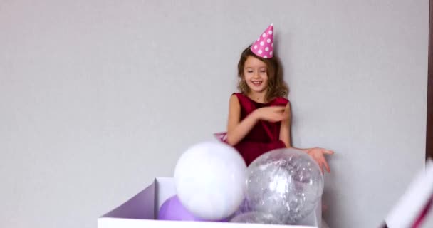 Radostná holčička v růžových šatech a klobouku otevřít velkou dárkovou krabici s balónky doma narozeninové party stuhy, Všechno nejlepší k narozeninám. Oslava - Záběry, video