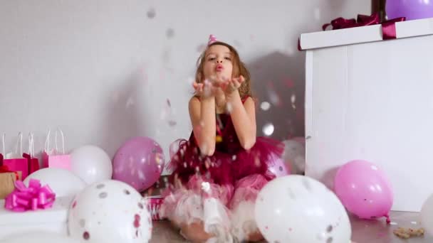 Powolny ruch piękna dziewczynka wysadza wielokolorowe confetti, bawiąc się w domu urodziny. Wszystkiego najlepszego. - Materiał filmowy, wideo