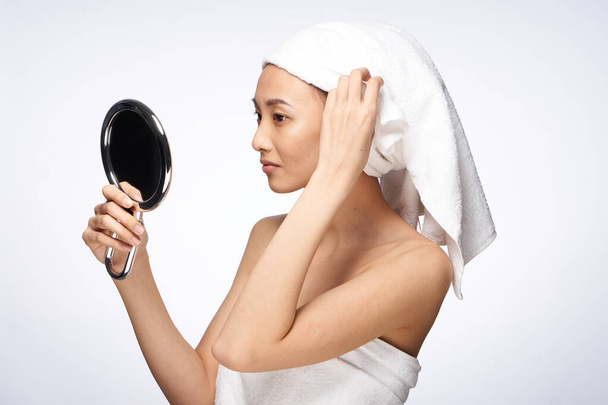 femme regarde dans le miroir avec une serviette sur la tête après douche soins de la peau style de vie - Photo, image