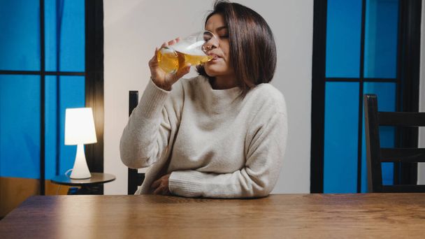 中年のアジアの女性は自宅のリビングルームでのビデオ通話を介して幸せな夜のパーティーイベントをオンラインでお祝いしてビールを飲んでいます。社会的距離コロナウイルスの隔離。視点又はPOV. - 写真・画像