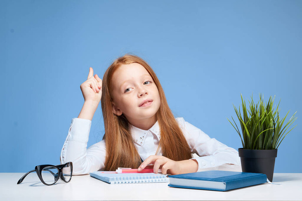 rudowłosa dziewczyna przy biurku, która uczy się w szkole. - Zdjęcie, obraz