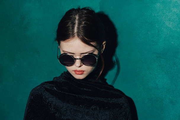 woman on a green background in a black sweater and sunglasses makeup - Photo, Image
