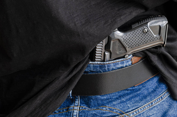 Hided handgun under the denim belt. A person is hiding a handgun under the denim belt. - Photo, Image