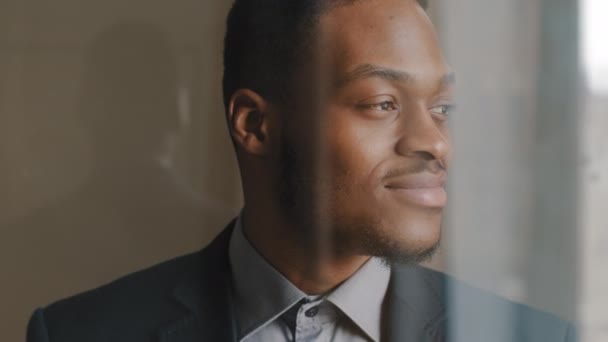Zicht vanuit raam door glas dromerig duur afro-Amerikaanse zakenman op zoek naar kant dromen planning toekomst overweegt ideeën projecten glimlachen oprecht op camera zwaaien knikt hoofd in overeenstemming - Video