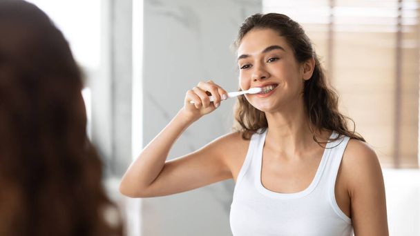 Ευτυχισμένη κυρία βούρτσισμα δοντιών με οδοντόβουρτσα στέκεται στο μπάνιο Εσωτερική - Φωτογραφία, εικόνα