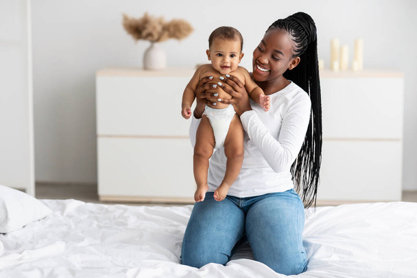 Negro mamá sentado en la cama con su lindo bebé - Foto, imagen