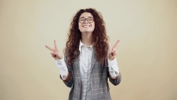 De vrolijke jonge vrouw met haar tanden uit toont het gebaar van vrede met beide handen. - Video