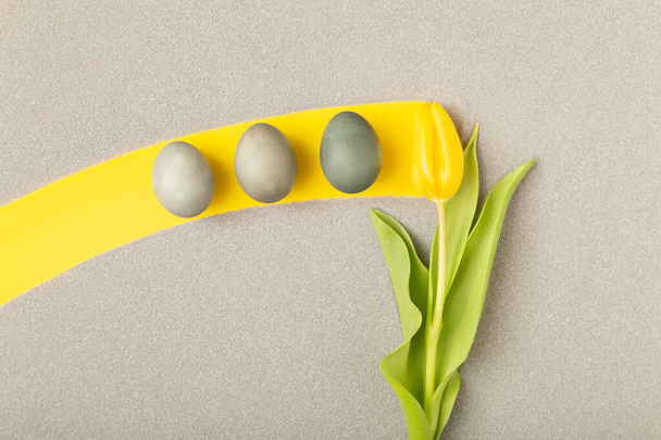 Huevos de Pascua grises en raya amarilla hechos por tulipán en arena. - Foto, imagen
