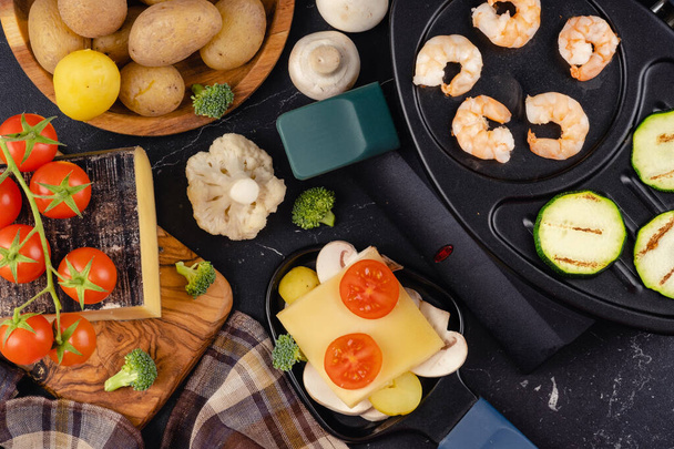 Delicious traditional Swiss melted raclette cheese on chopped boiled potatoes with vegetables. - Photo, image