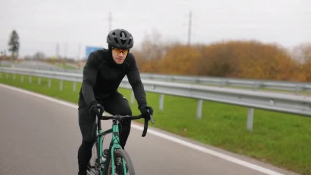 De sporter traint op de fiets. Hij rijdt op de snelweg in het koude seizoen. Hij kleedt zich in warme kleding. 4K - Video