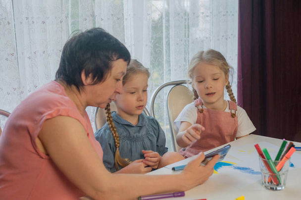 Бабушка показывает две внучки урок рисования по телефону домой - Фото, изображение