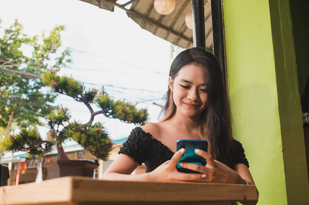 Onnellinen nuori aasialainen nainen kiireisesti tekstailee tai chattailee puhelimessa. Al fresco kahvilassa. - Valokuva, kuva