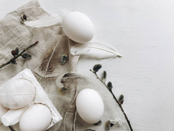 Natural easter eggs, soft feathers, pussy willow branches on white rustic table. Flat lay with space for text. Simple stylish rural Easter still life. Modern aesthetics, pastel beige and grey colors - Photo, Image