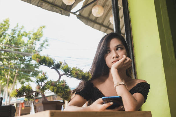 Uma mulher asiática entediada e sem tesão segura um telefone possivelmente cansado de navegar em suas mídias sociais ou esperar por alguém. - Foto, Imagem